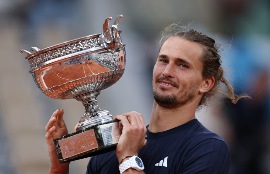 Man holding a large ornate silver trophy up to camera, celebrating victory on court.