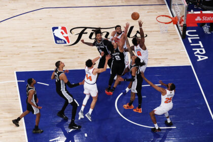 Basketball players leap for a loose ball under the hoop during a game on a wooden court with 'Finals' logo visible.