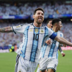 Argentinian soccer player celebrating with arms wide on the field in a blue-and-white striped jersey (number 10).