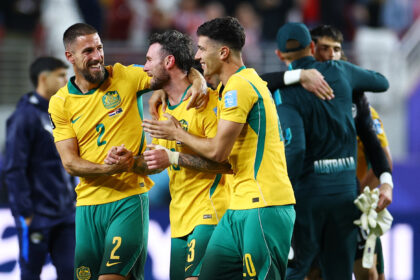 Australian soccer players in yellow and green celebrate with arms around each other on the field.
