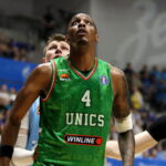 Basketball player in a green UNICS jersey looks up during a game, with a crowd in the background.