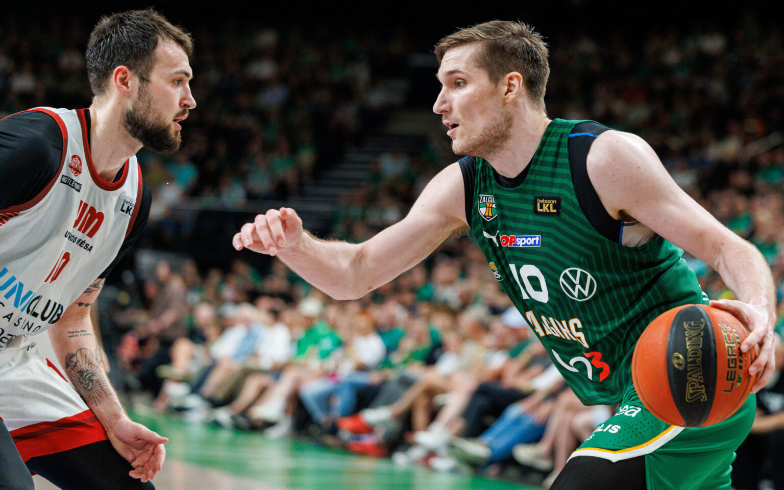 Two basketball players in action: a white-jersey guard facing a green-jersey defender with the ball at the sideline.