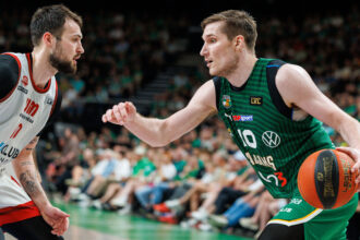 Two basketball players in action: a white-jersey guard facing a green-jersey defender with the ball at the sideline.