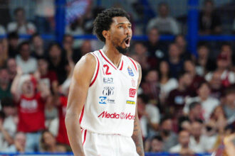 Basketball player in a white jersey with number 2, shouting with mouth open, on a crowded arena backdrop.