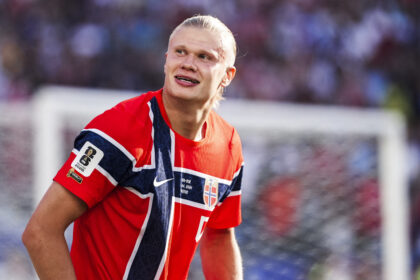 Male athlete in a red, white, and blue Norwegian jersey, looking to the left on a sports field.