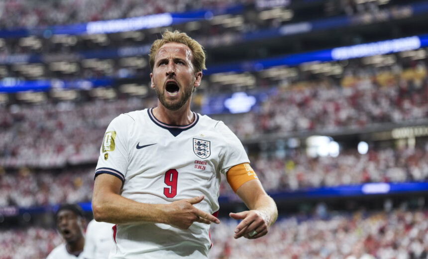England forward in a white jersey with number 9, celebrating a goal amid a packed stadium crowd