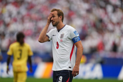 England national team forward with hand on forehead on the pitch, crowd blurred in background.