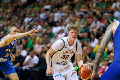 Lithuanian player in white jersey (#32) dribbles the ball as a Ukrainian defender in blue reaches out in a crowded arena crowd behind them