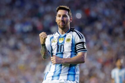 Male soccer player in Argentina national team jersey celebrates on the field, fist raised in triumph.