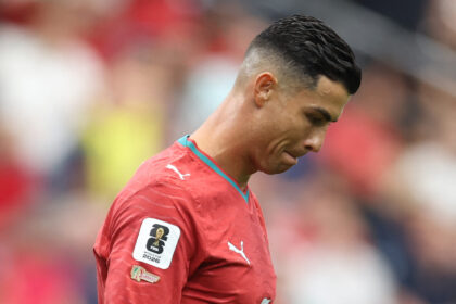 Side profile of a footballer in a red jersey looking downward, with a FIFA World Cup 2026 badge on the sleeve