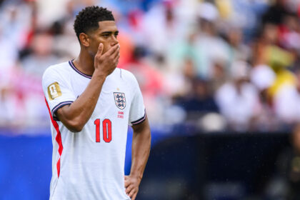 Soccer player in England jersey with hand over mouth, standing on the field during a match.