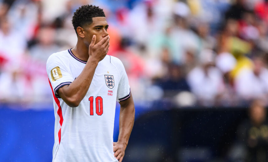 Soccer player in England jersey with hand over mouth, standing on the field during a match.