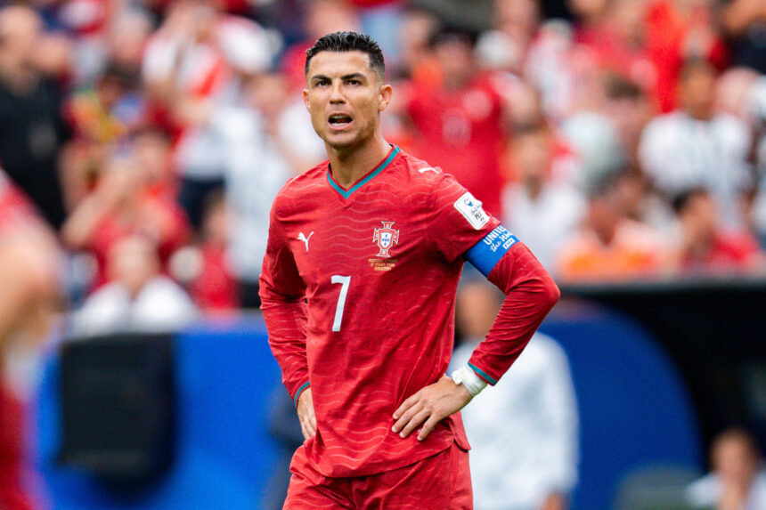 Male soccer player in a red Portugal kit with captain's armband, standing on a crowded field during a match.
