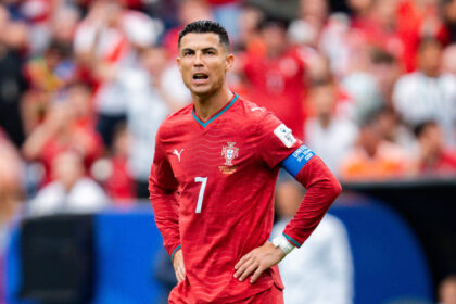 Male soccer player in a red Portugal kit with captain's armband, standing on a crowded field during a match.