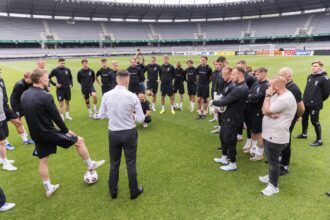 Soccer team standing in a circle on the pitch listening to the coach during training.