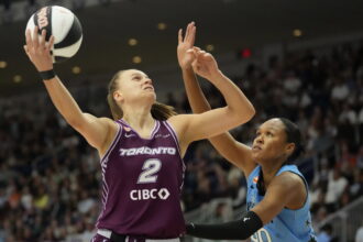 Basketball player in a purple Toronto jersey (no. 2) reaches for the ball as a blue-uniform defender guards nearby with a crowded arena in the background.