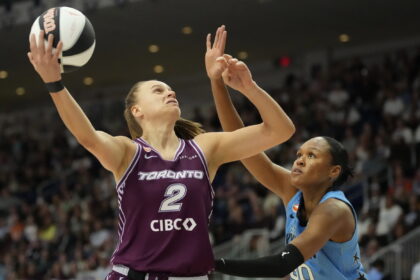 Basketball player in a purple Toronto jersey (no. 2) reaches for the ball as a blue-uniform defender guards nearby with a crowded arena in the background.