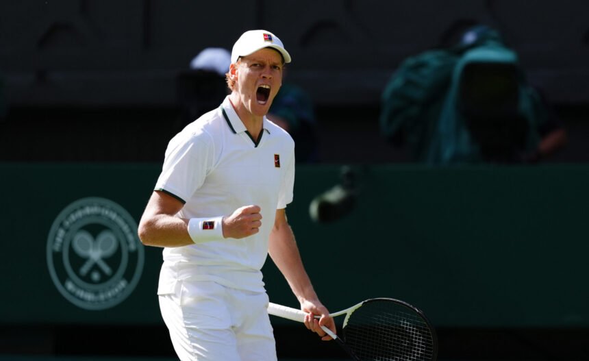 Tennis player in white outfit shouting during a match, holding a racket in front of a dark backdrop, sweat and intensity visible on his face.