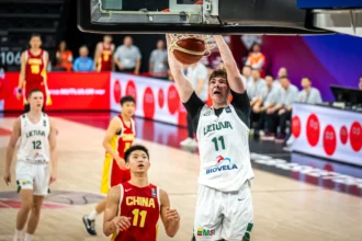 Lithuanian player in white (#11) jumps to dunk near the hoop as Chinese players in red look on. Crowd and banners in the background.