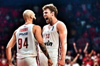 Two basketball players in white uniforms argue on the court, one shouting toward the other, with ‘FOURNIER’ and the number 34 visible on the back and a crowd in the background.