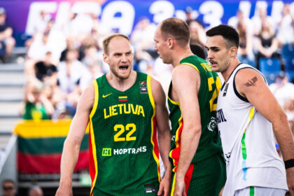Basketball players from Lithuania in green jerseys argue with a white-jersey opponent during a game, crowd watching in the background.