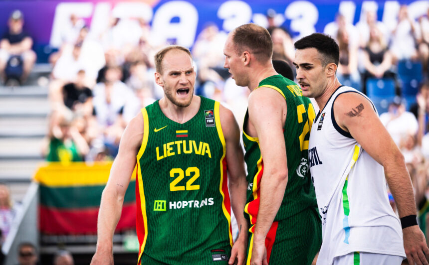 Basketball players from Lithuania in green jerseys argue with a white-jersey opponent during a game, crowd watching in the background.