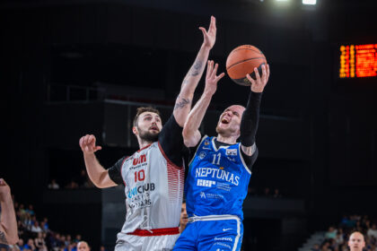 Two basketball players leap for the ball in a crowded arena, contesting a rebound.