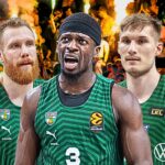 Three basketball players in green jerseys stand together on a court with a cheering crowd and flaming pyrotechnics behind them, celebrating.