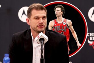 Man in a suit speaking at a press conference, microphone in front, with Chicago Bulls branding in the background with a Bulls cutout.