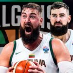 Two bearded basketball players celebrate on the court, one shouting with ball in hand, wearing white uniforms with green trim.