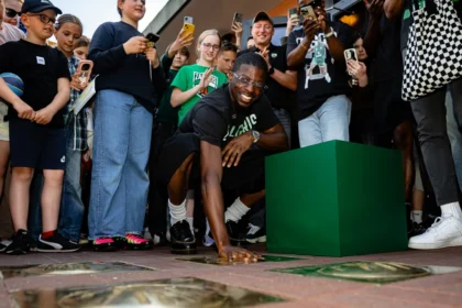 Crowd surrounds a breakdancer mid-mow under a green cube, capturing the moment on phones and cameras.
