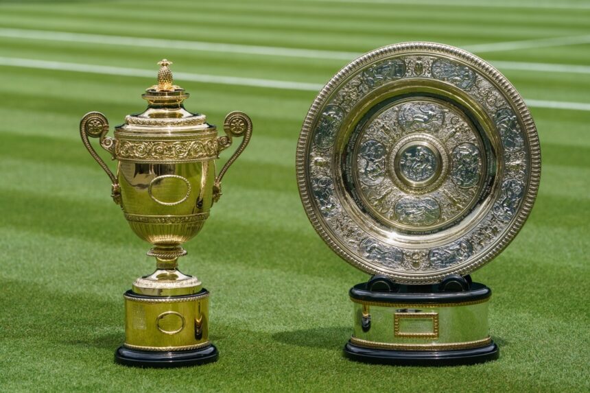 Two ornate gold trophies—a tall cup on the left and a large intricately engraved plate on the right—sit on a green grass sports field.