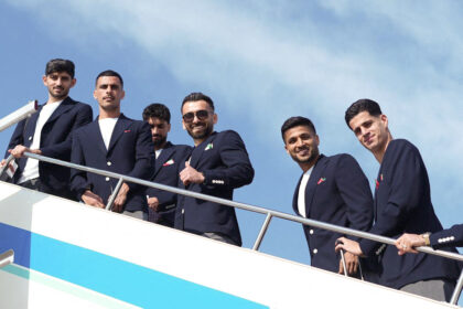 Six men in navy blazers posing on a yacht deck against a blue sky.