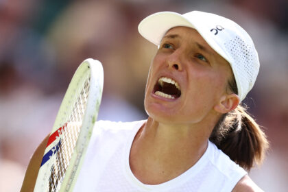 Female tennis player shouting with rackets near her face, wearing a white cap and shirt.