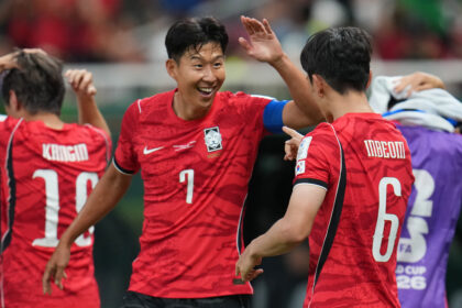 Korean footballers in red jerseys celebrate with high fives on the field. (team celebration)