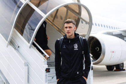 Young man in a black sports tracksuit stepping down from mobile stairs beside a white airplane at an airport.