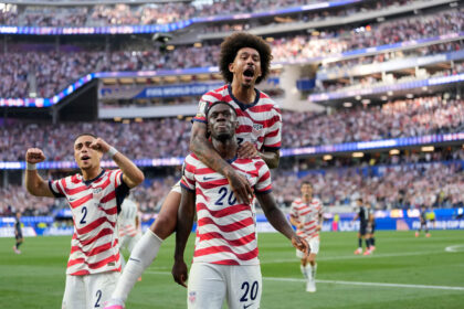 USA soccer players celebrate a goal on the field with jubilant crowd in background