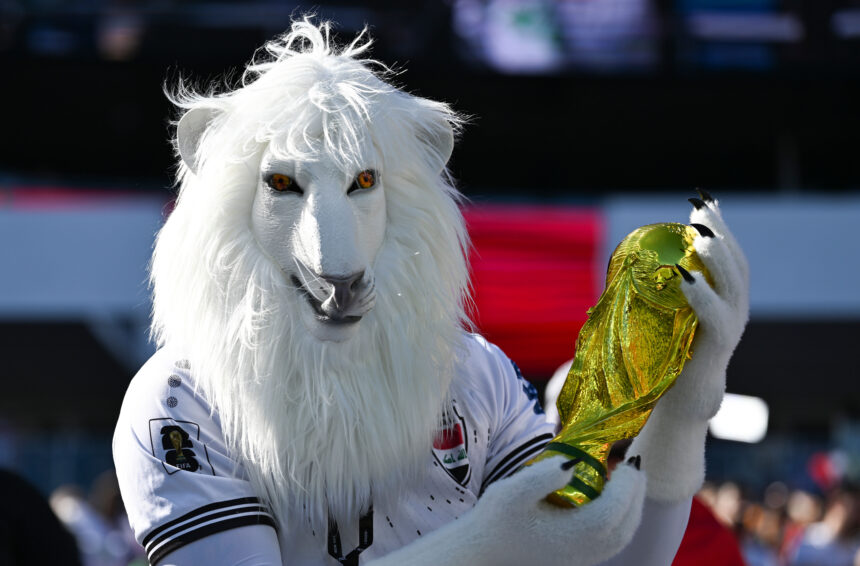White llama mascot in a white jersey, holding a shiny gold trophy at a stadium event.