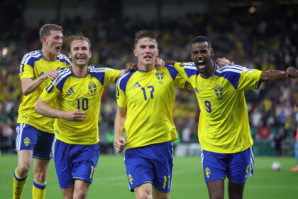 Sweden national football players celebrate together on the pitch, arms around each other in yellow uniforms.