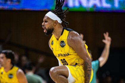 Basketball player in a yellow jersey with a white headband celebrates, running on court with a determined side profile.
