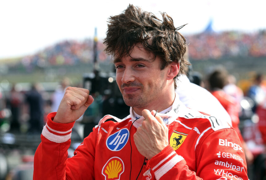 Male race car driver in a red Ferrari suit celebrating with fists raised at a crowded event at the track.