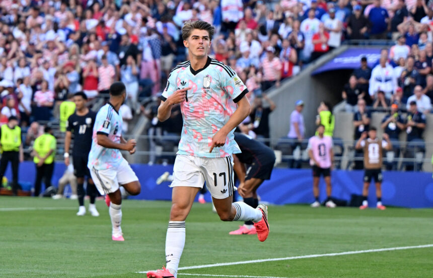 Soccer player in a light-blue patterned jersey runs on the field with a cheering crowd behind him.