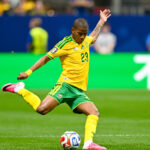 Brazil national team soccer player, number 23, in yellow kit kicking a ball on a green field during a match.