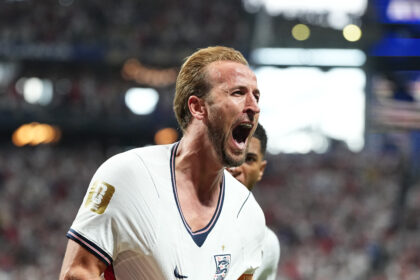 Footballer in England national team jersey celebrating on the pitch with mouth open in a roar of celebration.