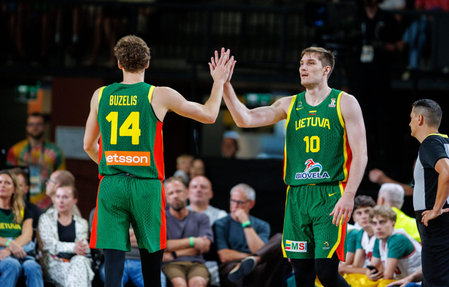 Two Lithuanian basketball players in green uniforms high-five on the court amid a crowd, #14 (Buzelis) and #10 (Lietuva).