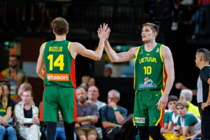 Two Lithuanian basketball players in green uniforms high-five on the court amid a crowd, #14 (Buzelis) and #10 (Lietuva).