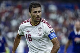 Spain national football team player in a white jersey with red trim (number 16) during a match on a stadium pitch.