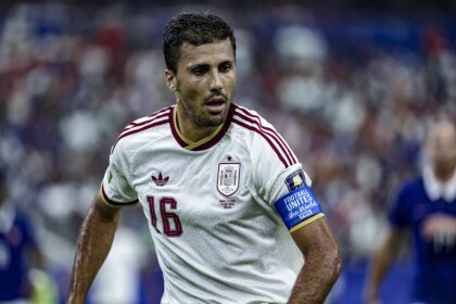 Spain national football team player in a white jersey with red trim (number 16) during a match on a stadium pitch.
