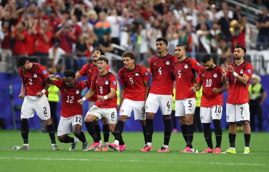 Group of football players in red jerseys celebrate on the field as fans cheer in the stands behind them.