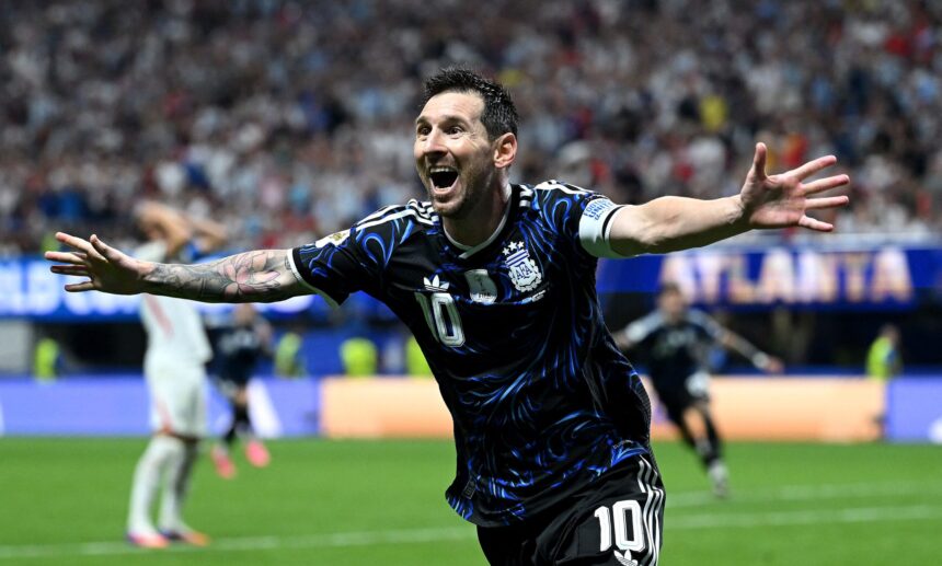 Soccer player in a blue-black jersey with number 10 celebrates with arms outstretched on the pitch amid a cheering crowd.